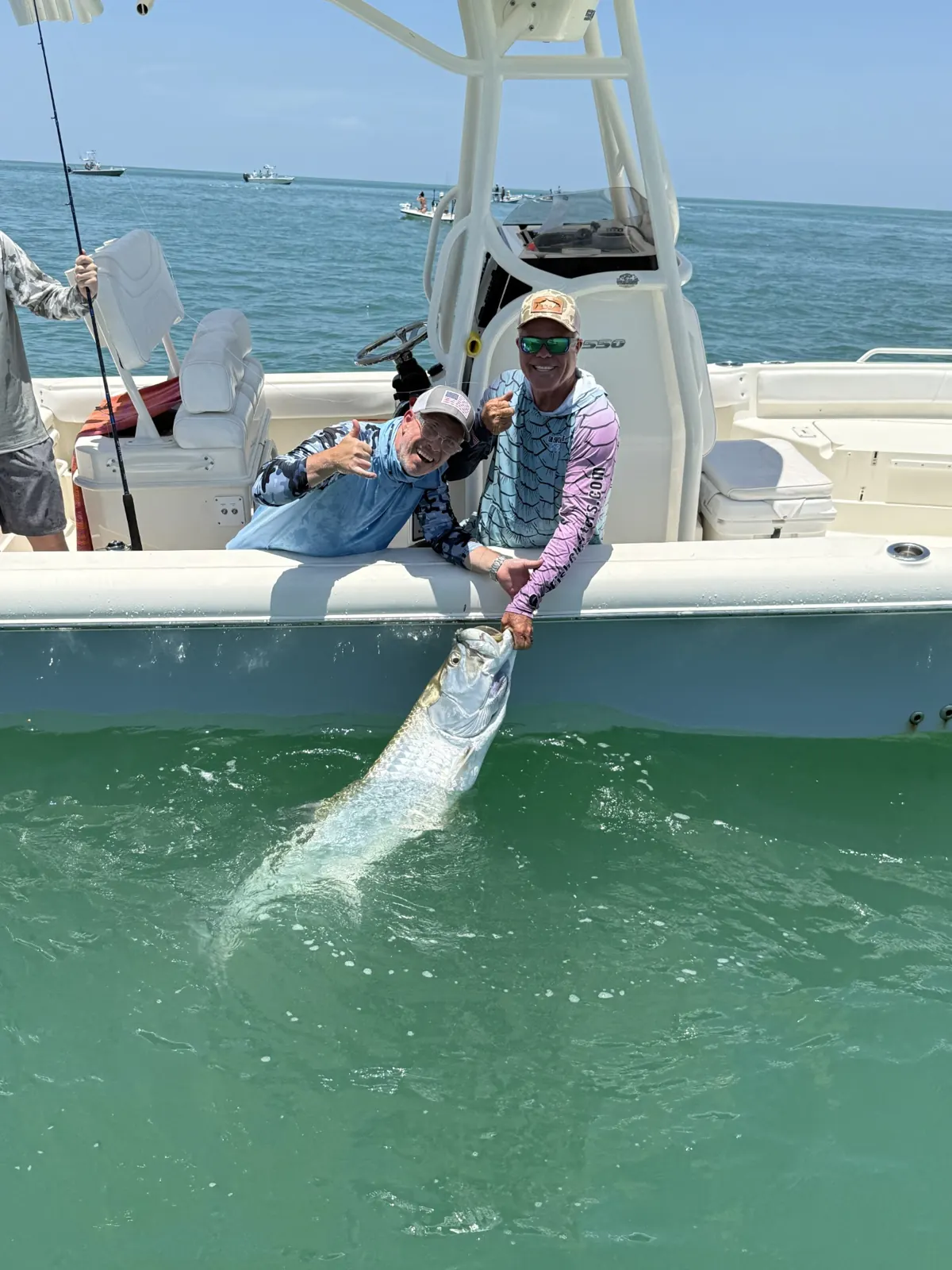 Two anglers beside a tarpon held in the water alongside the boat